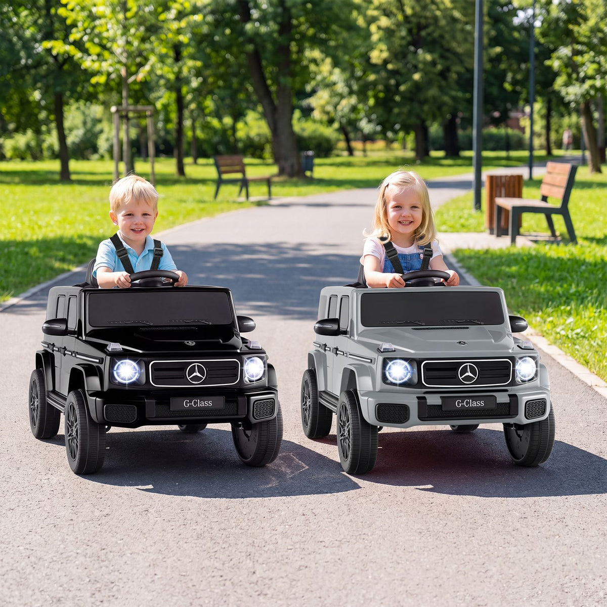 Two children drive black and white ride-on SUVs side by side on a park path.