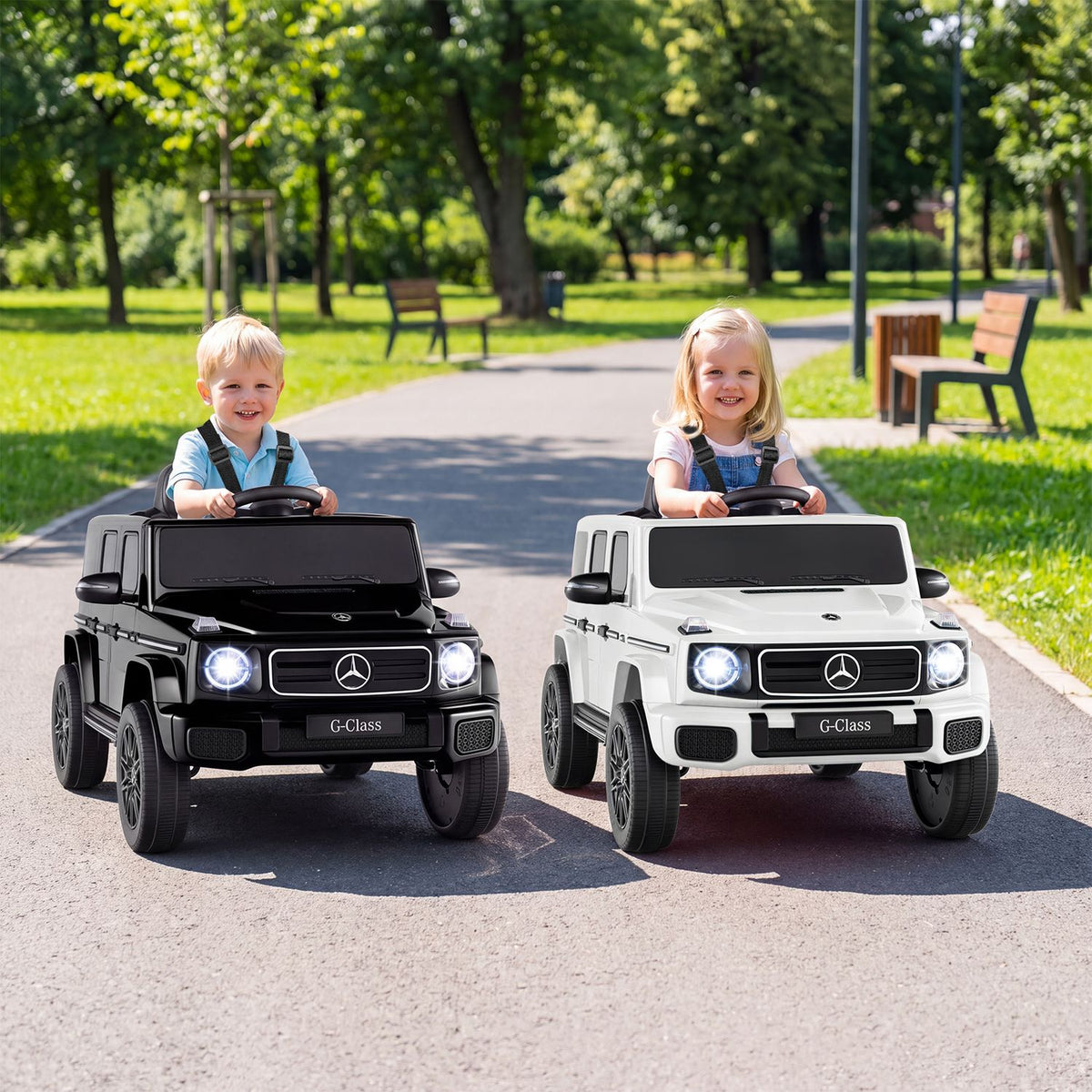 Two children sit in black and white miniature SUVs on a sunny park path.