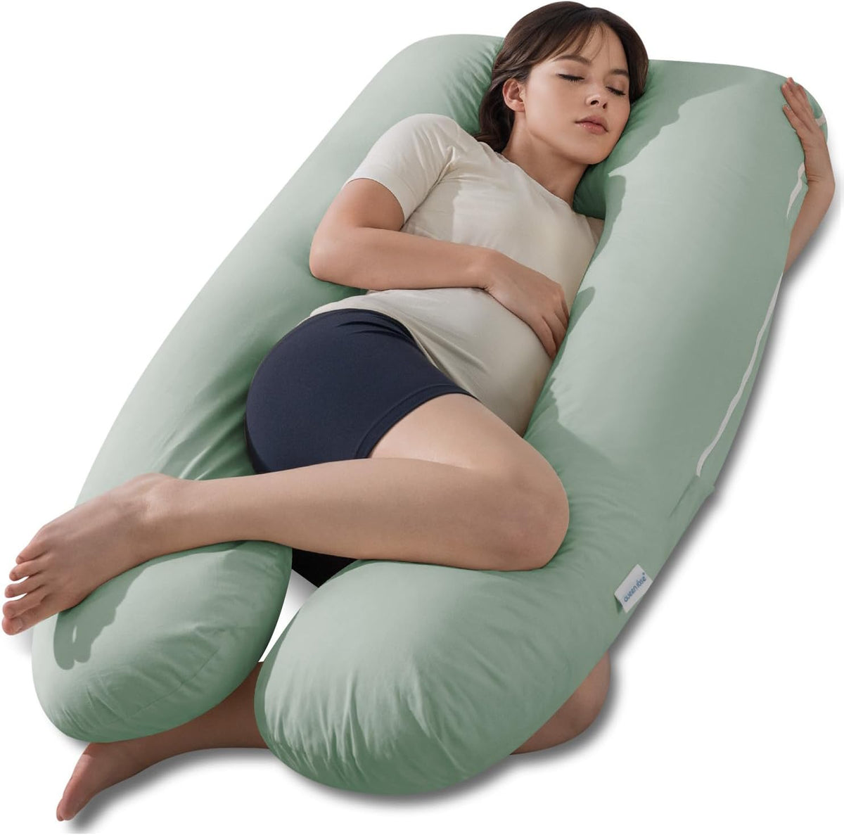 Woman resting inside a sage-green U-shaped maternity pillow with knees tucked between the sides.