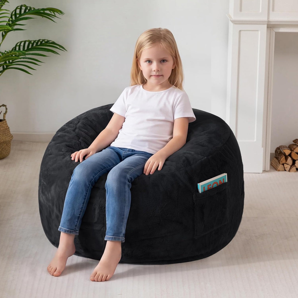 Child sitting on a black plush bean bag chair, a book visible in the pocket at the side.