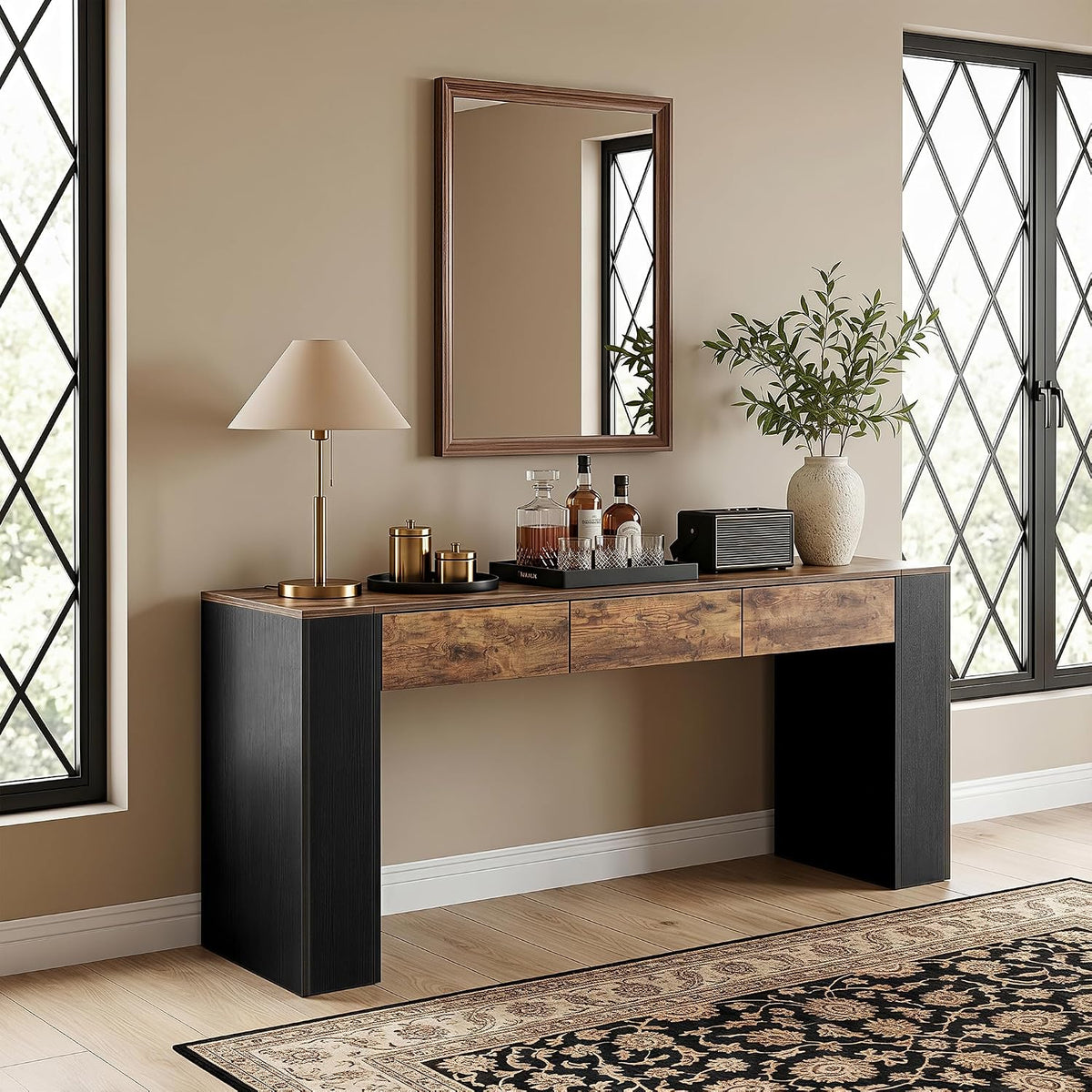 Console table styled in a bright entry with lamp, mirror, vase, tray of bottles, and patterned rug beneath.