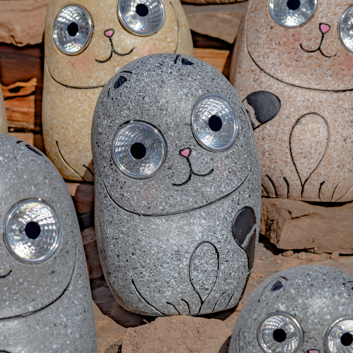 Several speckled stone-look cats with round reflective eyes sit among stacked rocks.