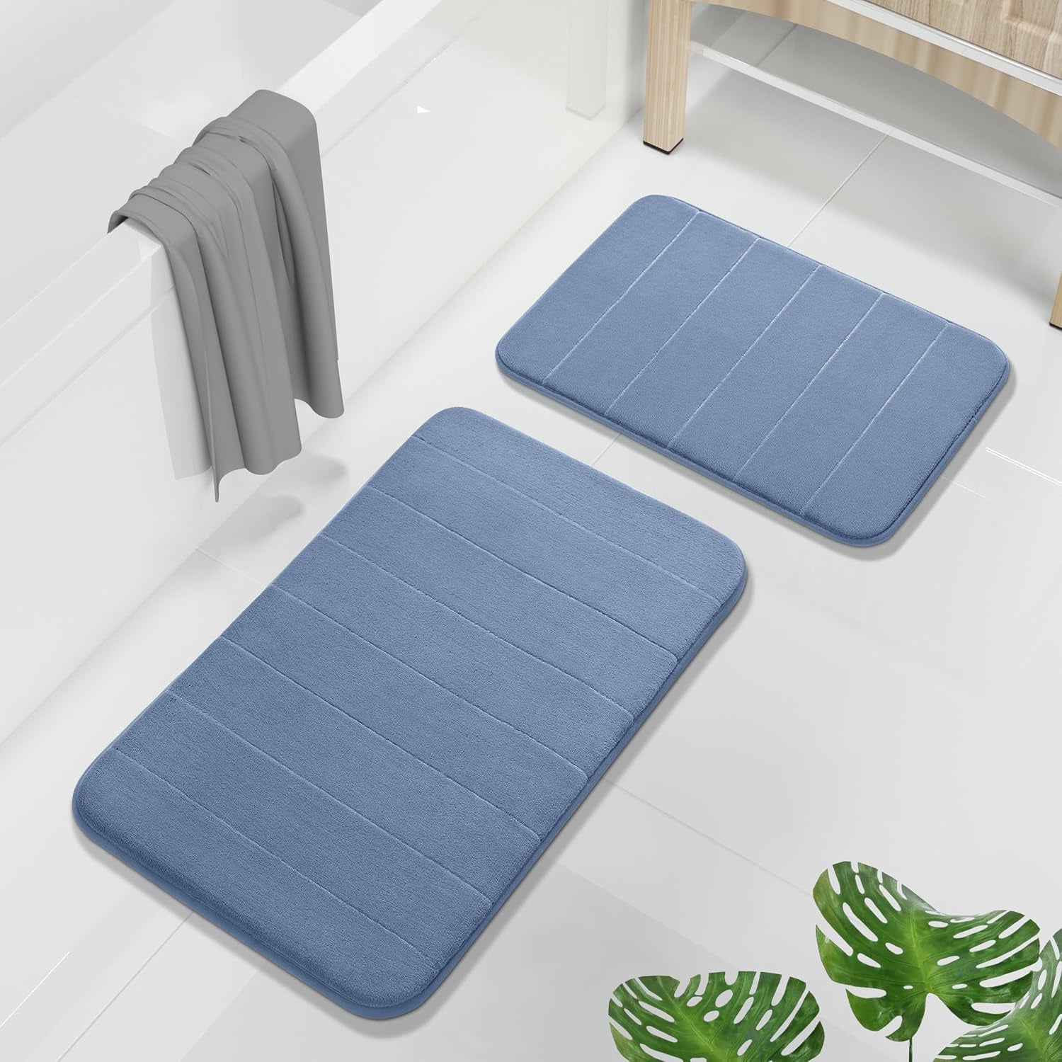 Two blue rectangular bath mats arranged near a bathtub on a white tile floor with a towel draped over the tub