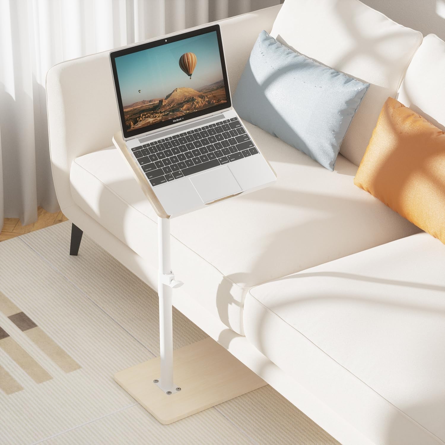 C-shaped tray table beside a white sofa with a laptop on the tilted surface, room setting view