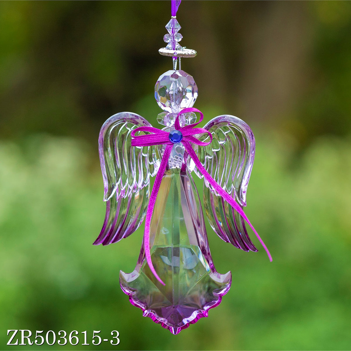 A hanging faceted angel ornament with curled wings and a fuchsia bow, shown against soft greenery.