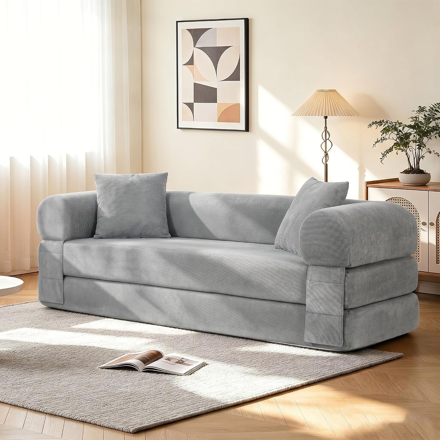 Light gray corduroy convertible sofa with two square pillows placed on a neutral rug in a bright room.