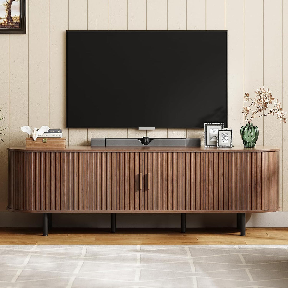 Walnut TV stand beneath wall-mounted TV showing closed tambour doors and decorative items on the top surface