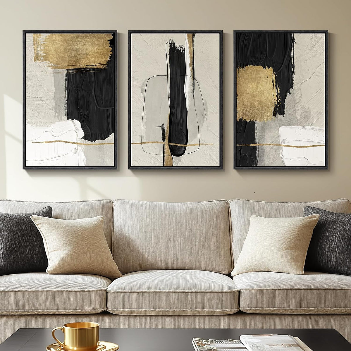 Three vertical framed abstract prints with black, white and gold accents hung above a beige sofa.