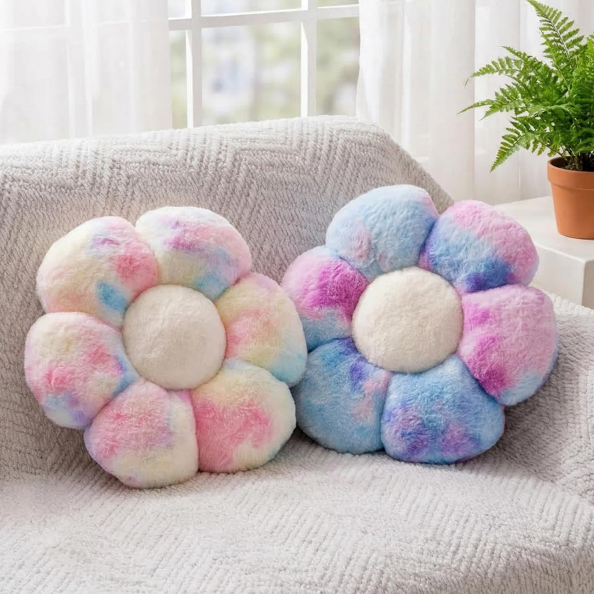 Two plush flower-shaped throw pillows in pastel tie-dye colors on a light textured sofa.