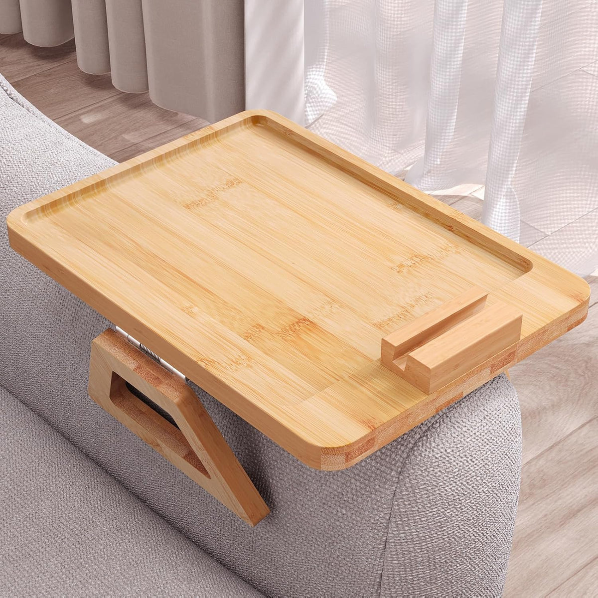 Natural bamboo tray mounted on a sofa arm, angled to show the clamp and wooden phone block at front