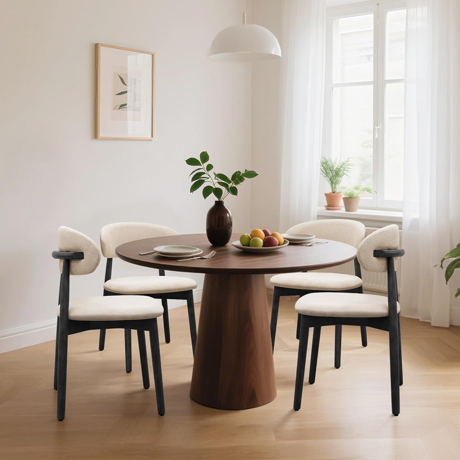 Four beige curved-back dining chairs with black frames surround a round table by a window.