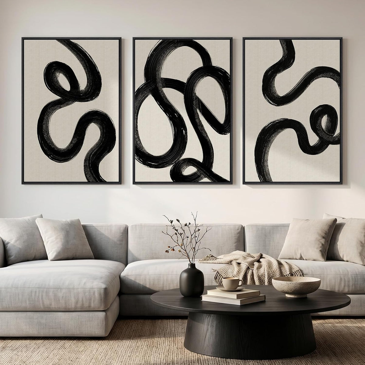 Three vertical canvases with looping thick black brushstrokes on a light background centered over a couch and coffee table.