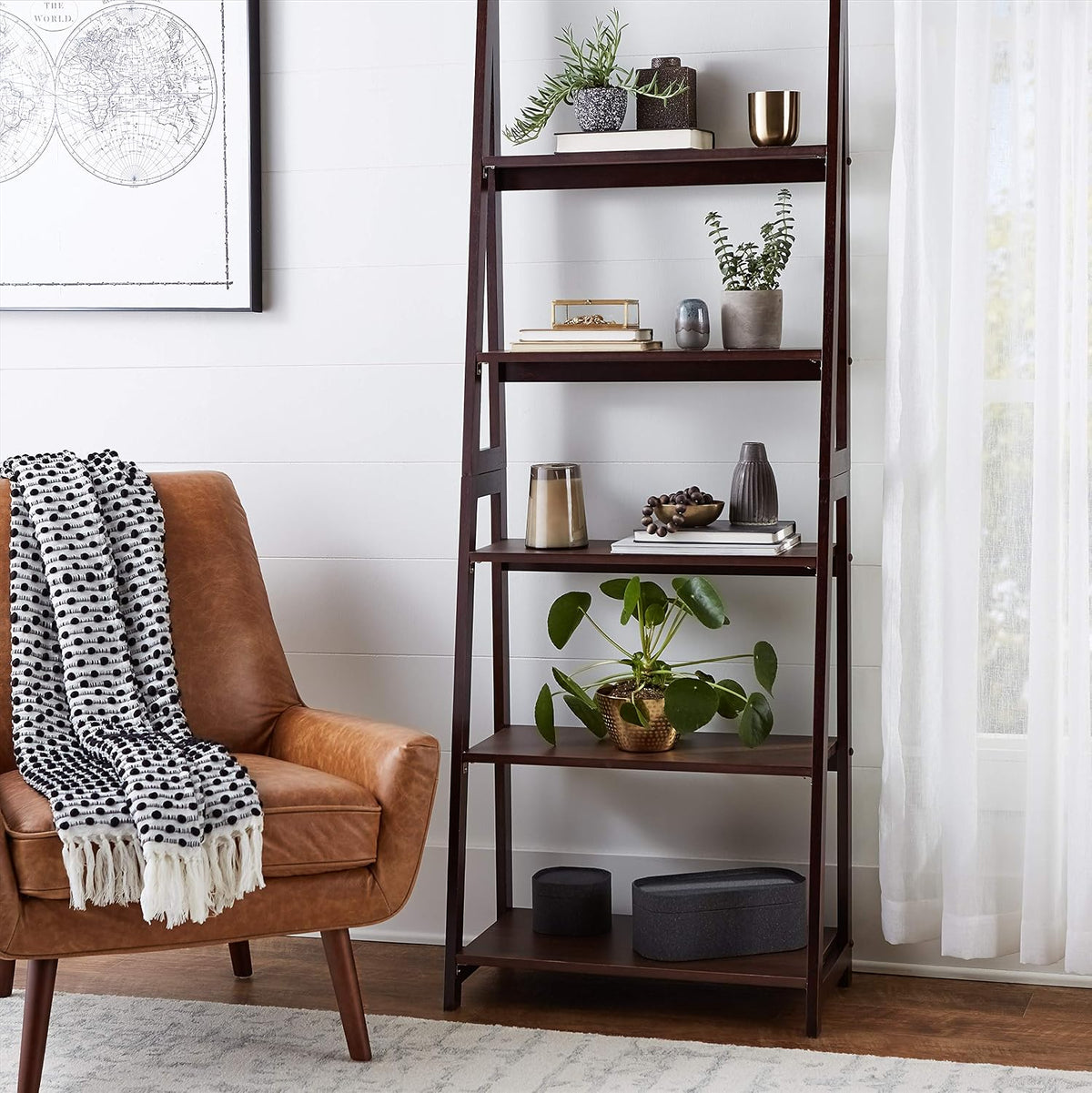 Styled living room scene with espresso ladder bookshelf beside a leather accent chair and decorative items on shelves