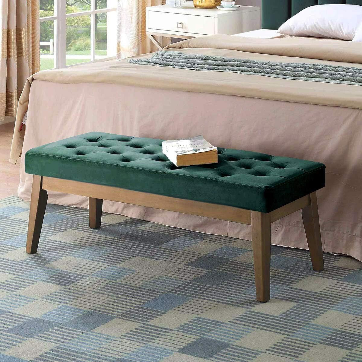 Three-quarter view of an emerald green tufted bench with a book on top at the foot of a bed.