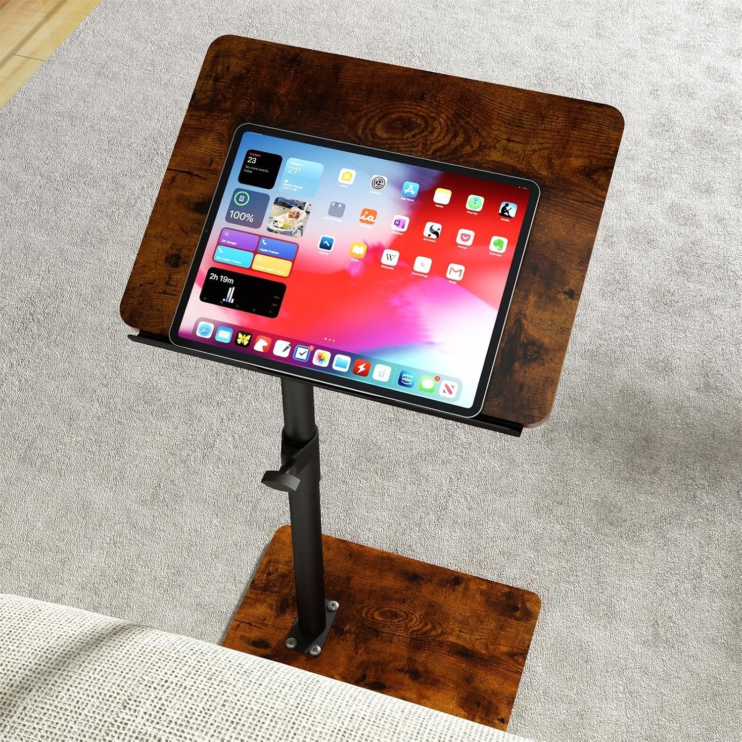 Dark wood tray table with black pole seen over carpet holding a tablet on its surface