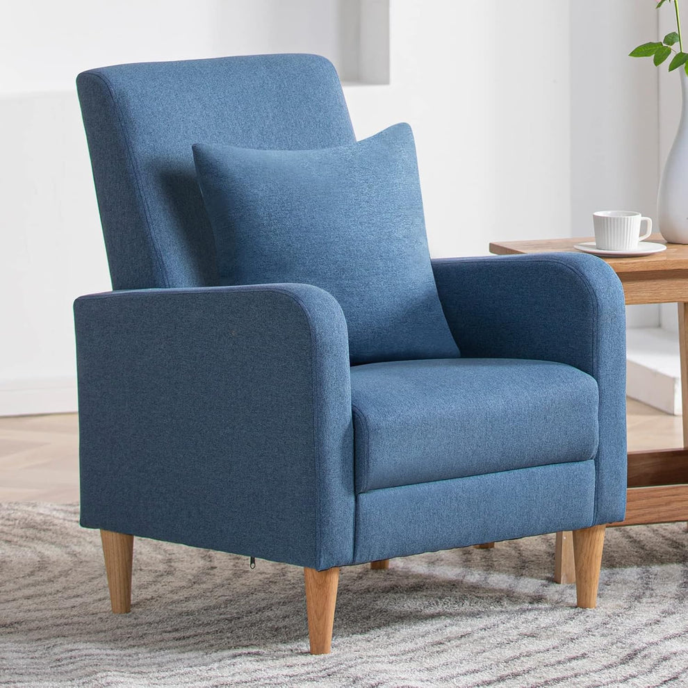 Blue high-back upholstered accent chair with matching square pillow on a rug next to a wooden side table and cup.