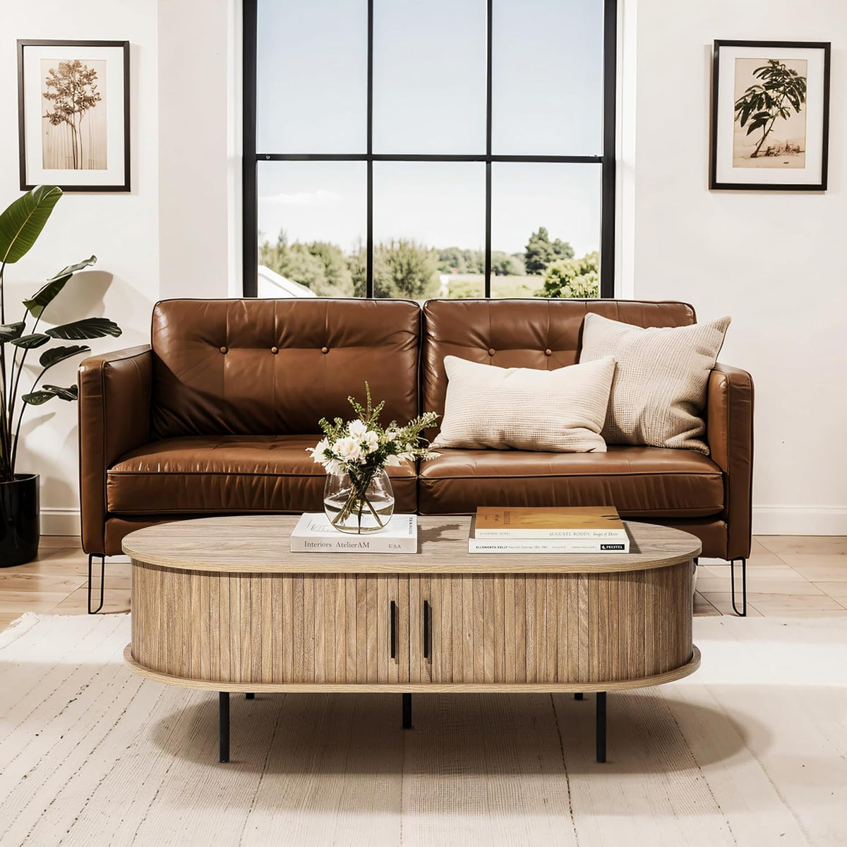 Oval coffee table centered before a leather sofa, showing tambour doors closed and slender black metal legs