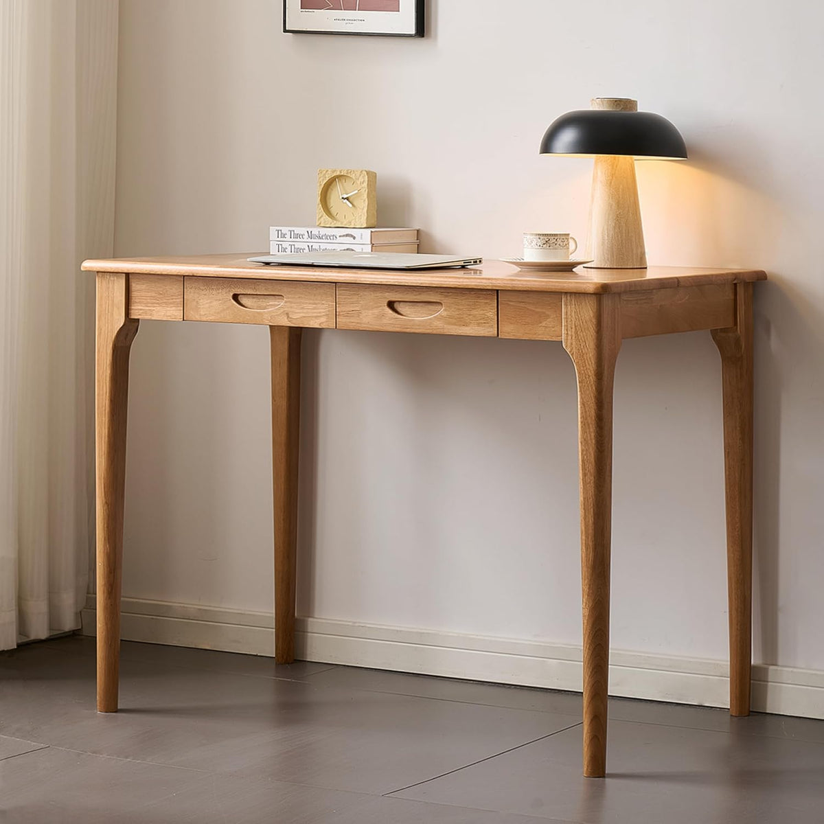 Front-facing shot of a lighter-finish wood desk with three drawer fronts and a table lamp on top.