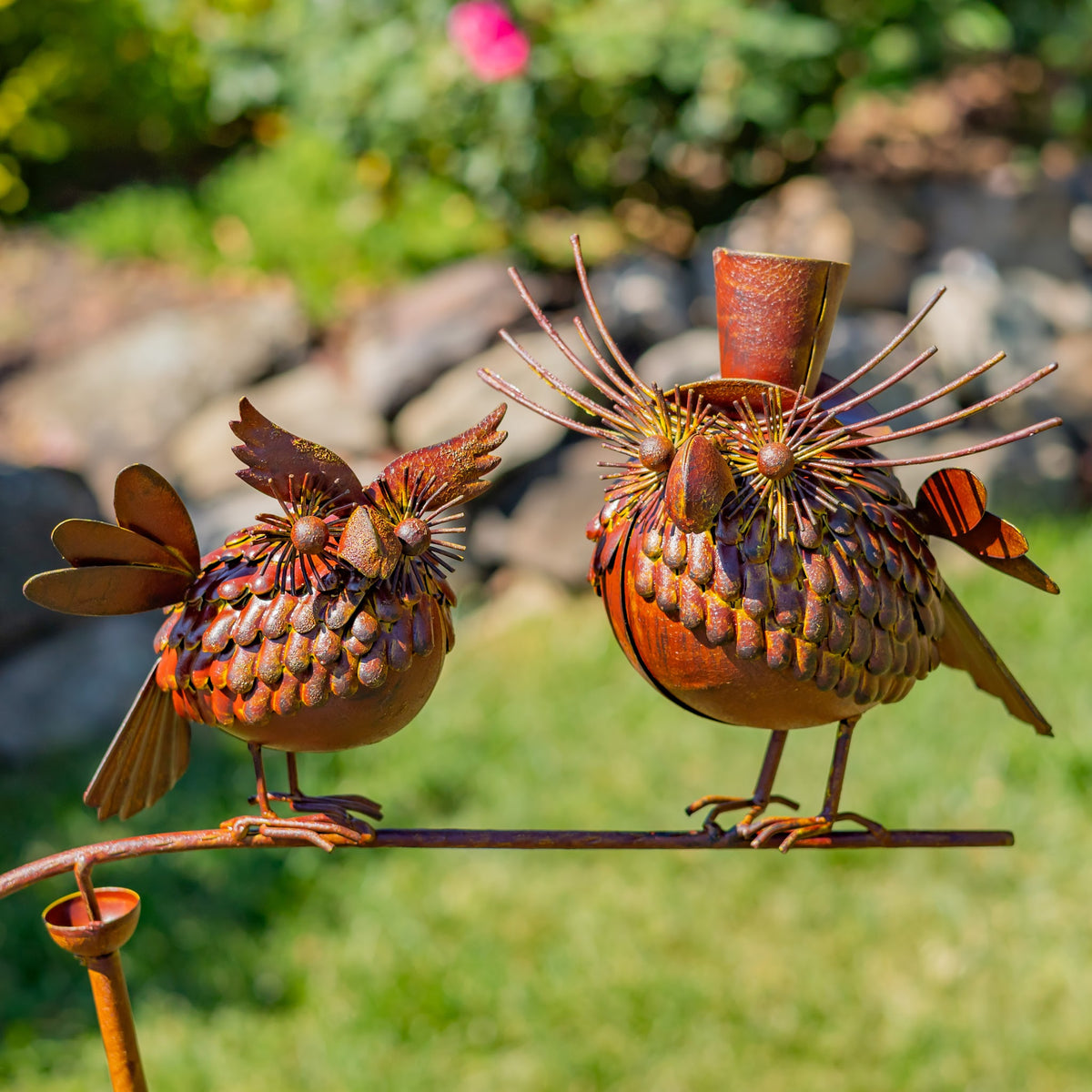 A closer view of two decorative metal birds perched on a balance stake outdoors.