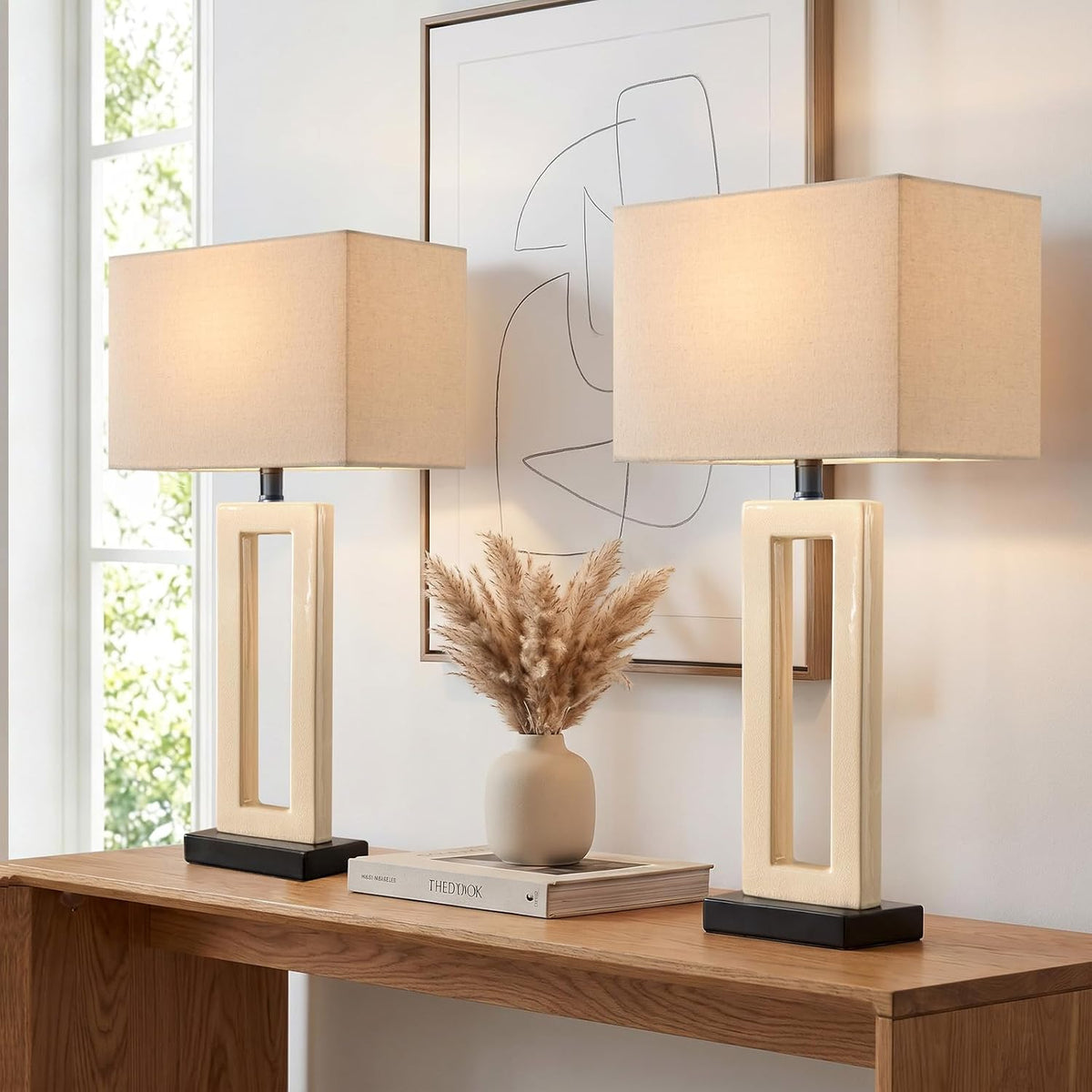 Two cream ceramic rectangular base lamps with linen rectangular shades on a wooden console with decor