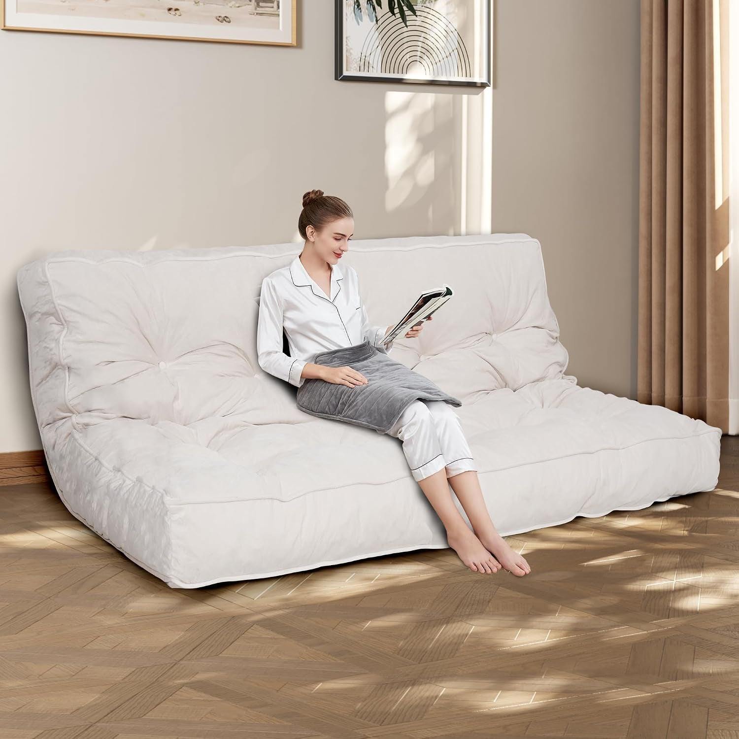 White futon mattress used as a low sofa with a person sitting and reading, angled room view