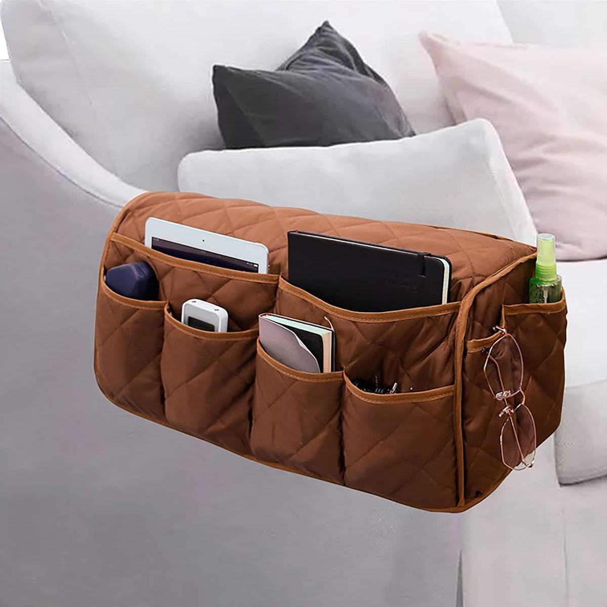 Quilted brown armrest organizer full of books, tablet and glasses hanging from a light sofa arm