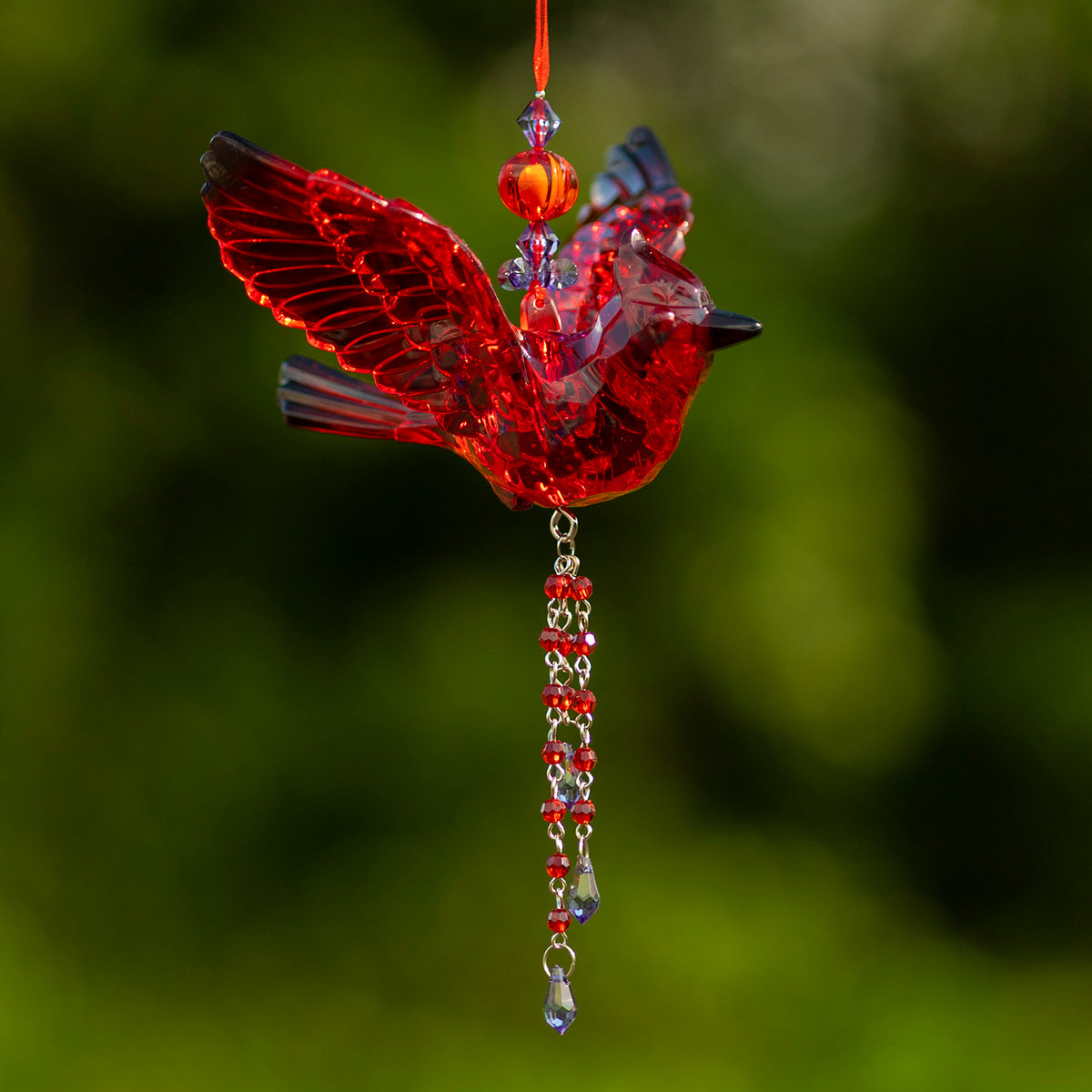 Red faceted bird ornament with one wing spread and a red-and-clear beaded tassel hanging below.