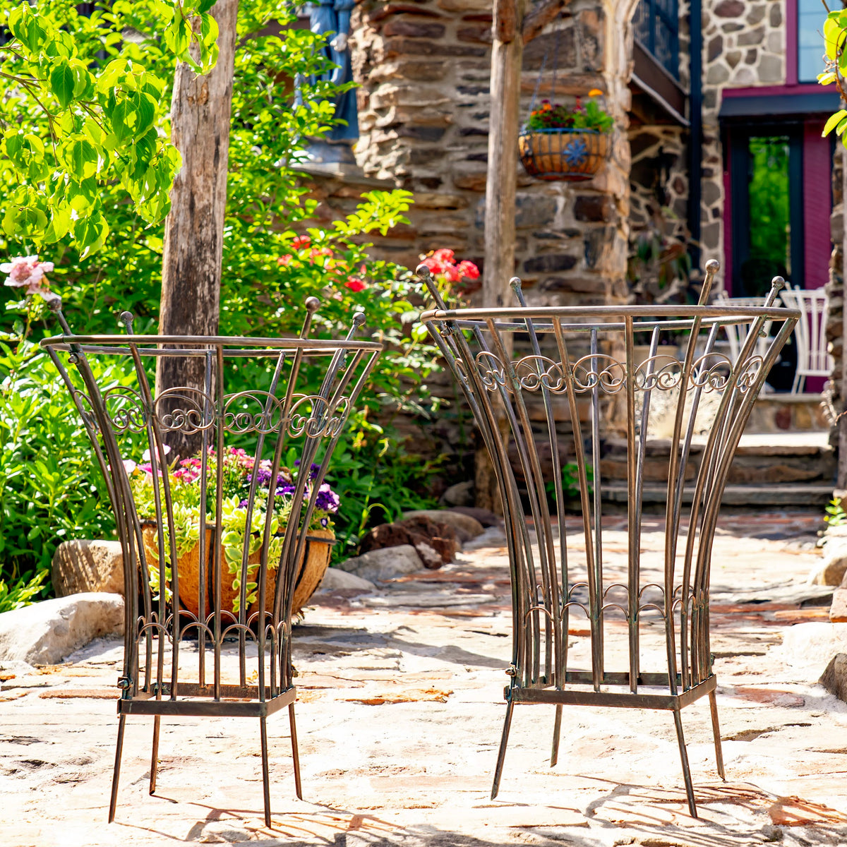 Two iron trellis stands on a stone garden path, with a potted flower arrangement in the smaller stand.