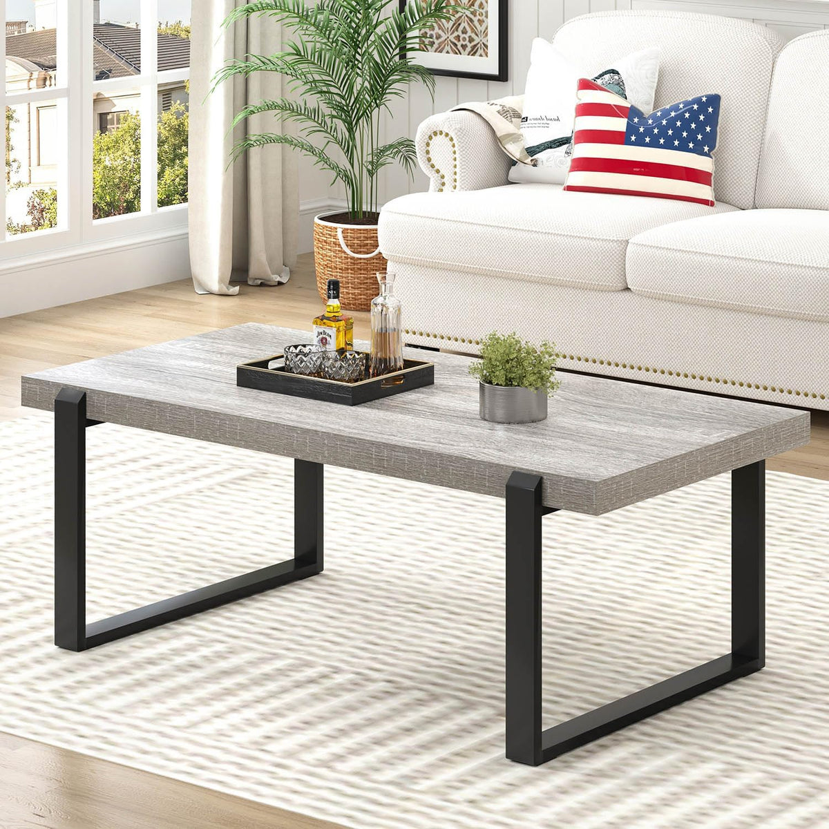 Light gray wood-grain tabletop with black metal legs positioned in front of a sofa and plant.