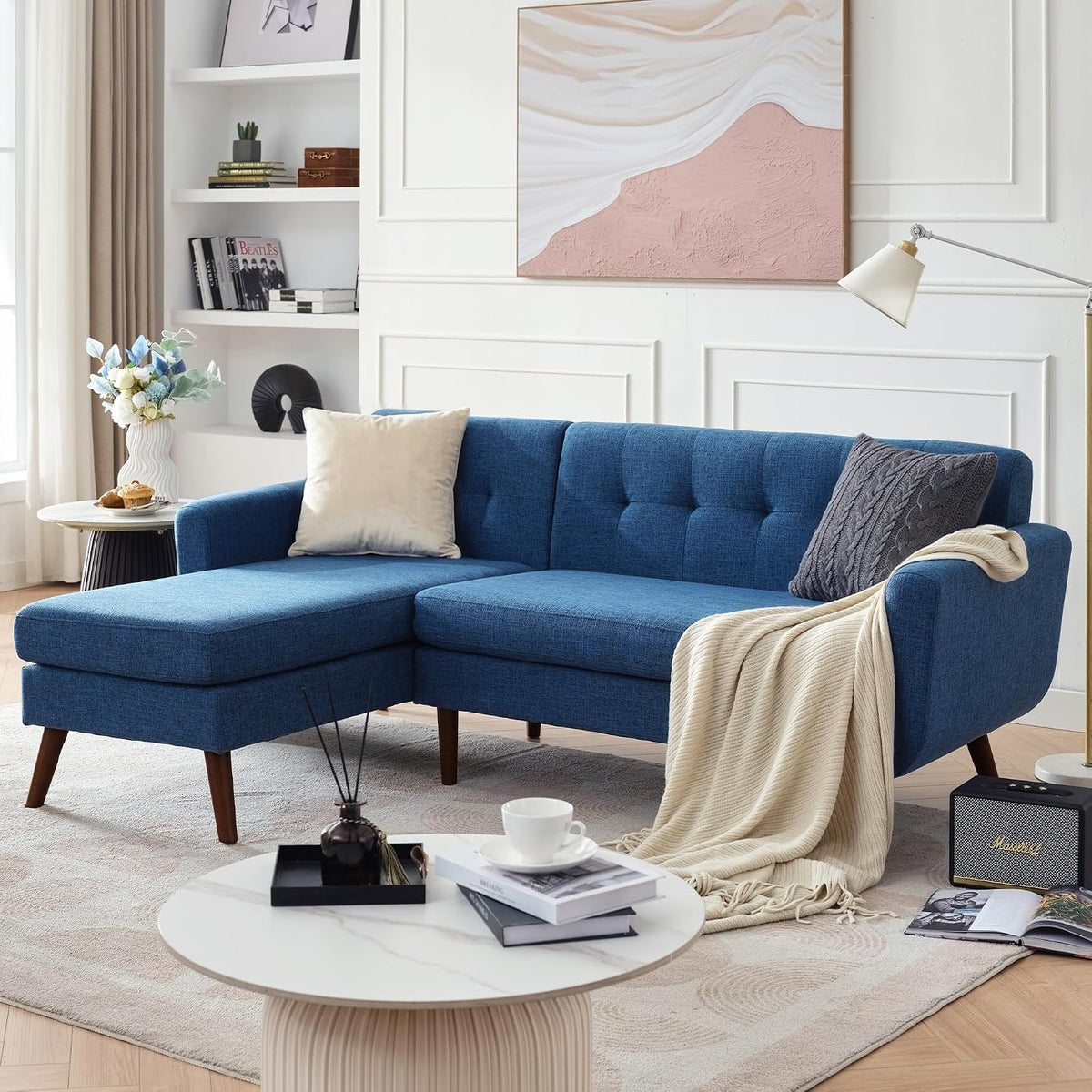 Blue tufted loveseat configured with a left chaise, wooden legs and a draped throw in a cozy room.