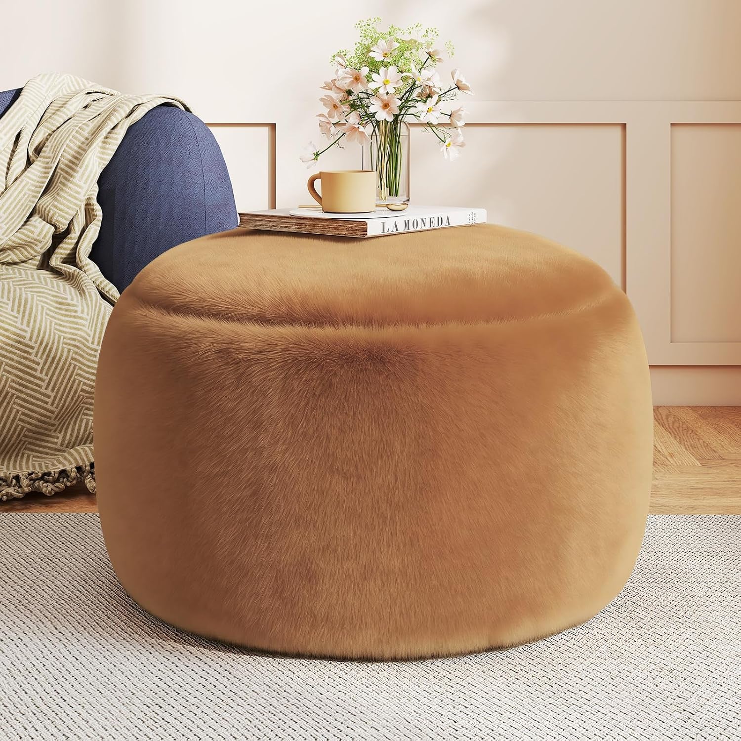 Close crop of a white faux-fur round pouf ottoman with book and vase on top