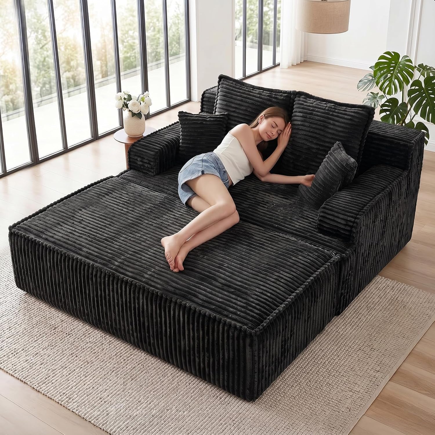 Top-front view of a dark gray corduroy chaise bed with pillows and a woman lying on it