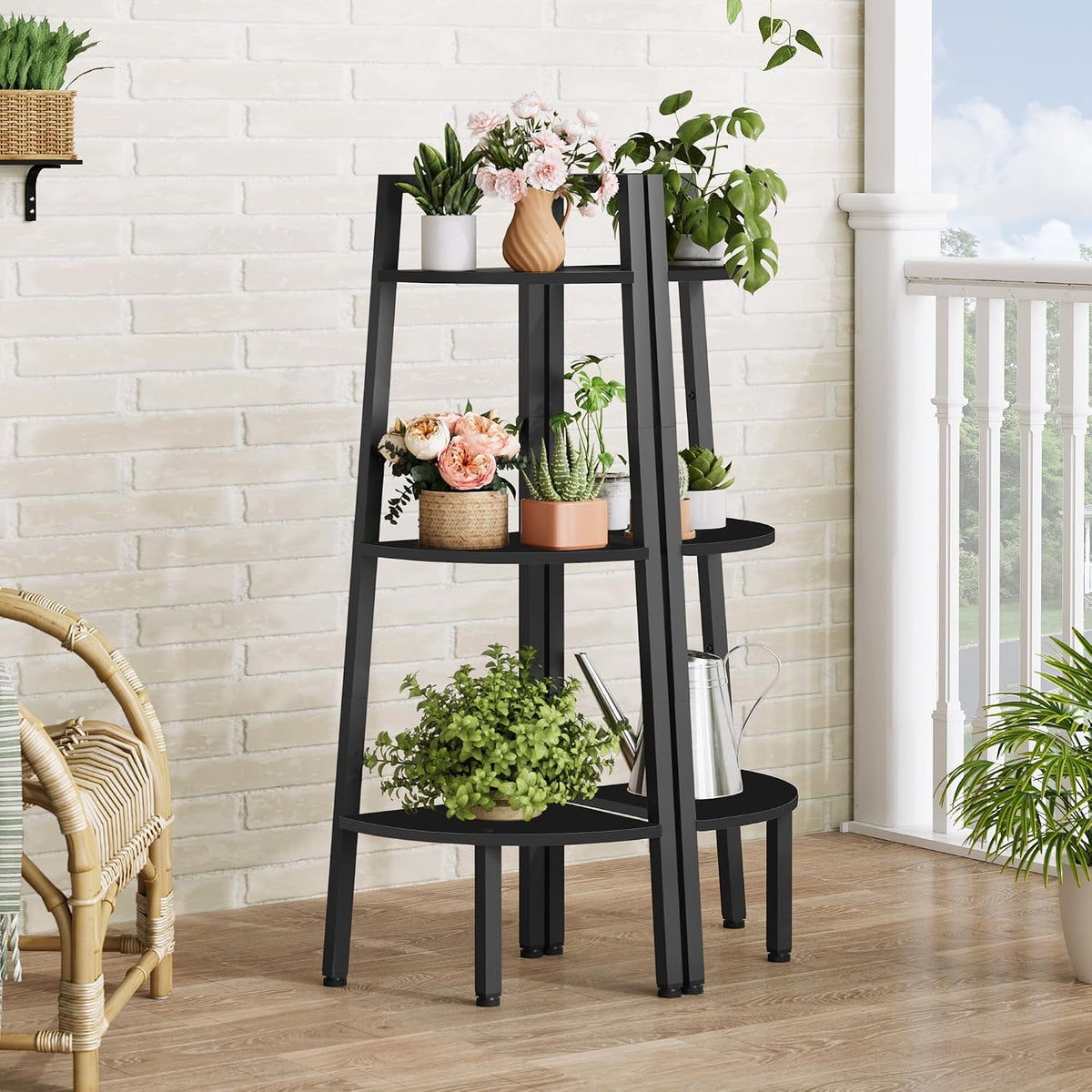 Three-tier black corner ladder shelf by a bright porch railing, each tier holding potted plants and a metal watering can.