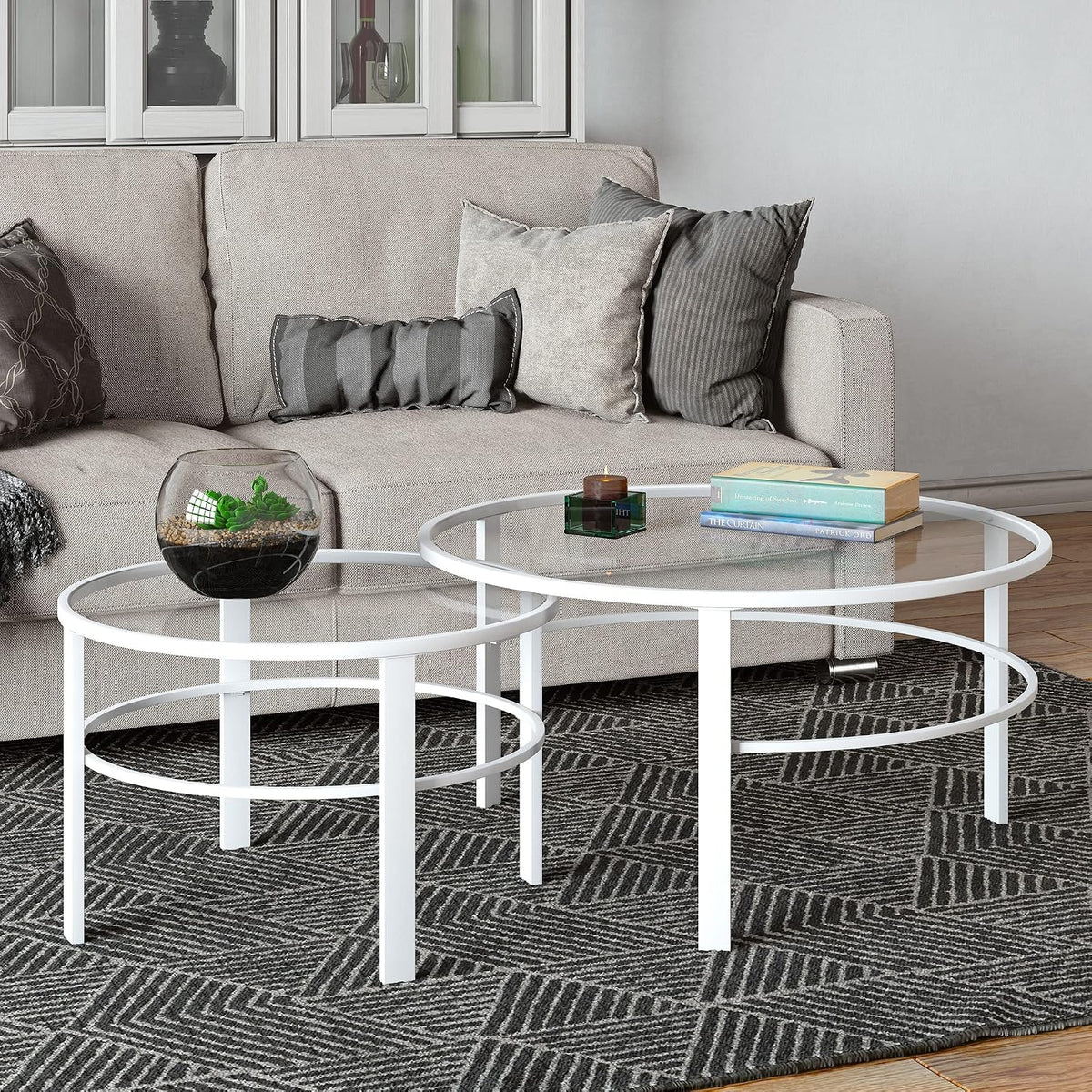 White nesting tables beside a light sofa with a glass terrarium on the smaller table and a stack of books on the larger.
