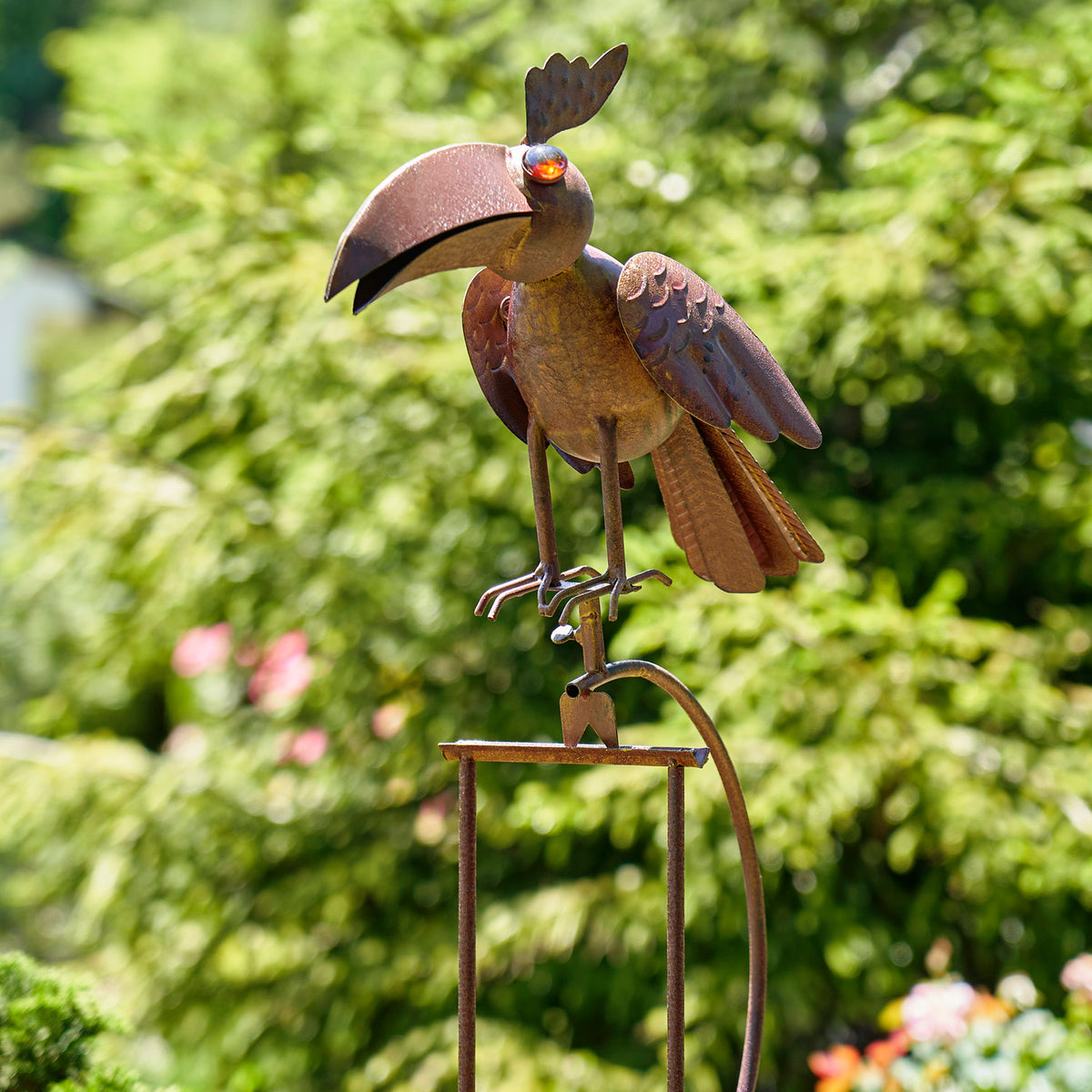 Rust-colored metal raven garden stake with a colorful glass eye, perched above a small hanging swing frame.