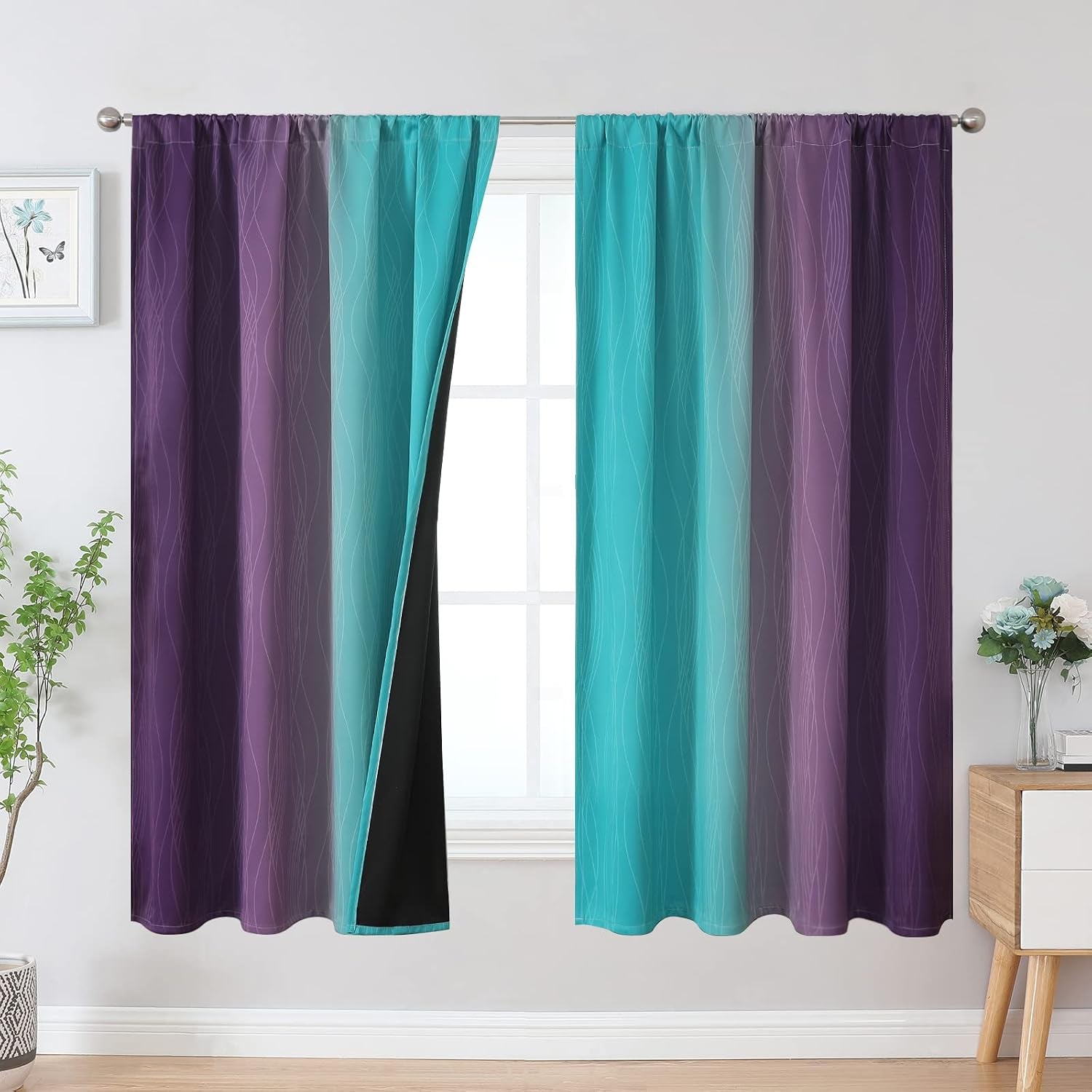 Window with two ombre curtains in teal and purple tones pulled on a rod showing black blackout lining.