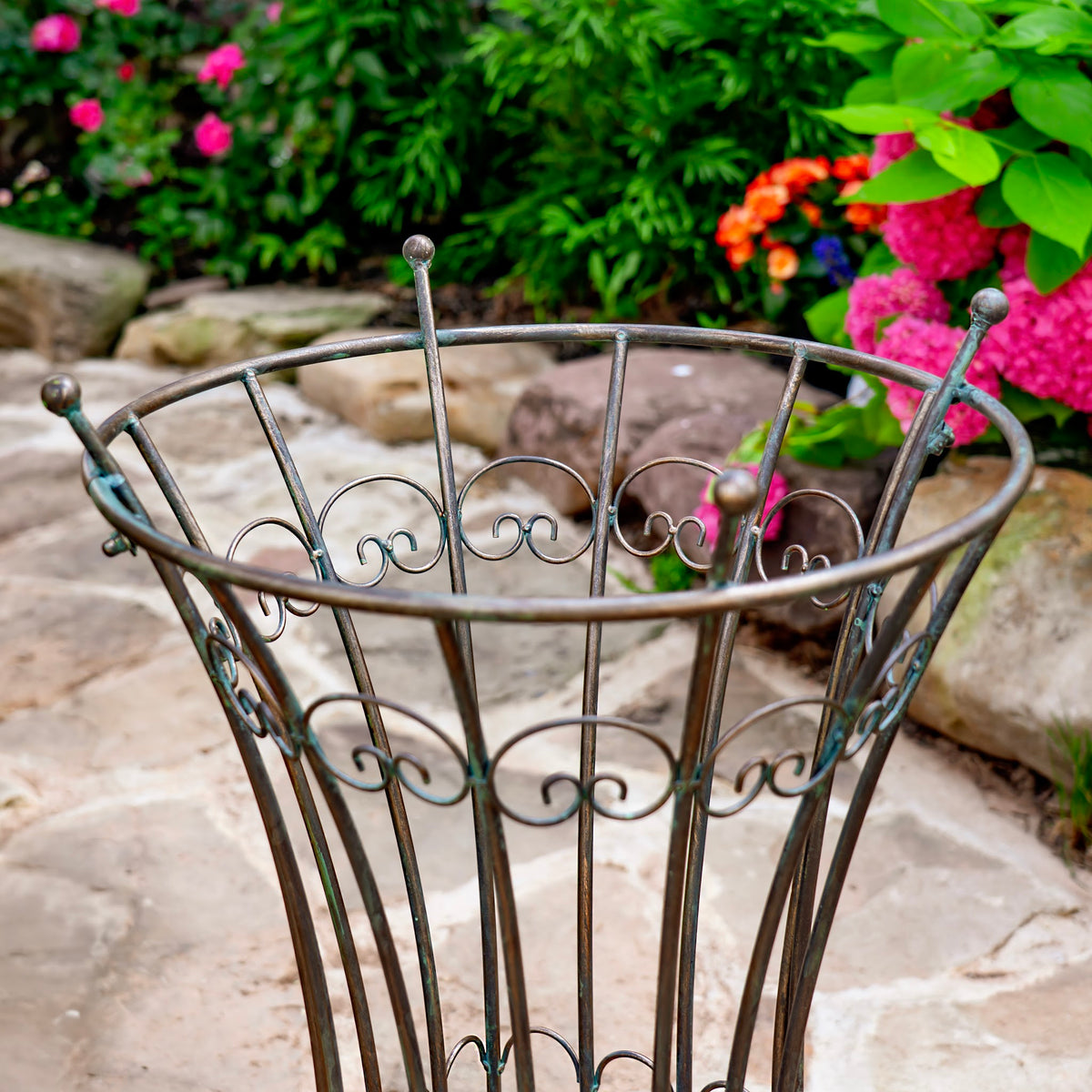 Close view of a bronze-toned iron garden stand with curved scrollwork and a round upper rim.