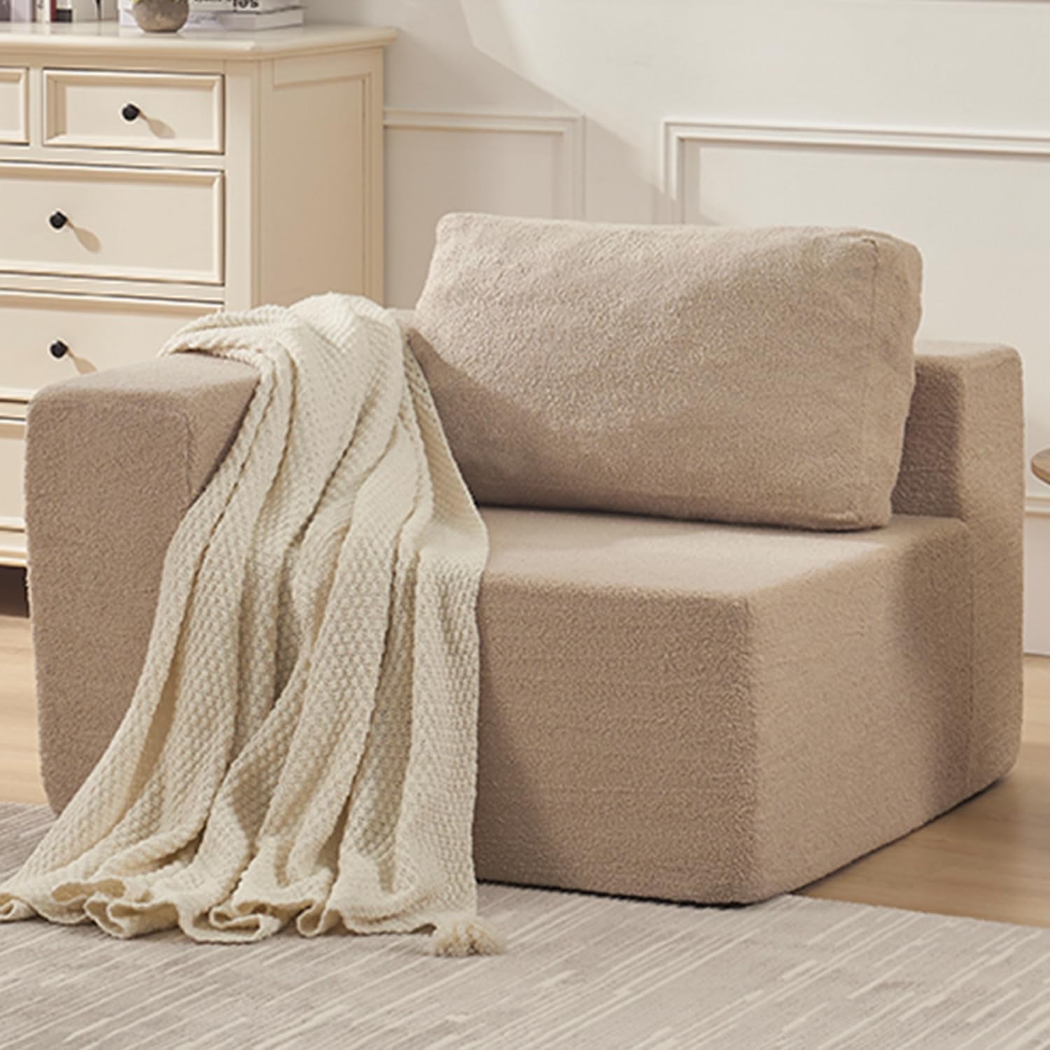 Single beige modular sofa corner module with low arm, back cushion and a cream throw draped over the arm.