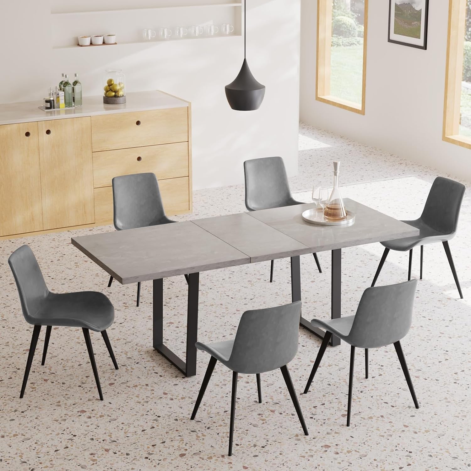 Concrete-look rectangular table top with U-shaped black metal legs and matching gray chairs in a sunlit room.