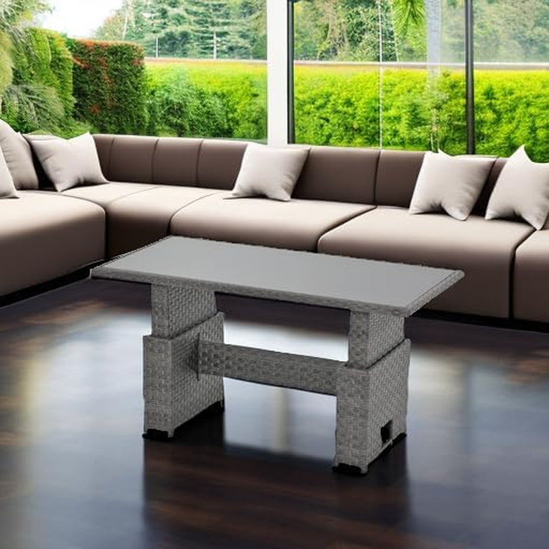 Grey resin wicker rectangular table with glass top shown lowered in a bright indoor living-room scene with sectional sofa