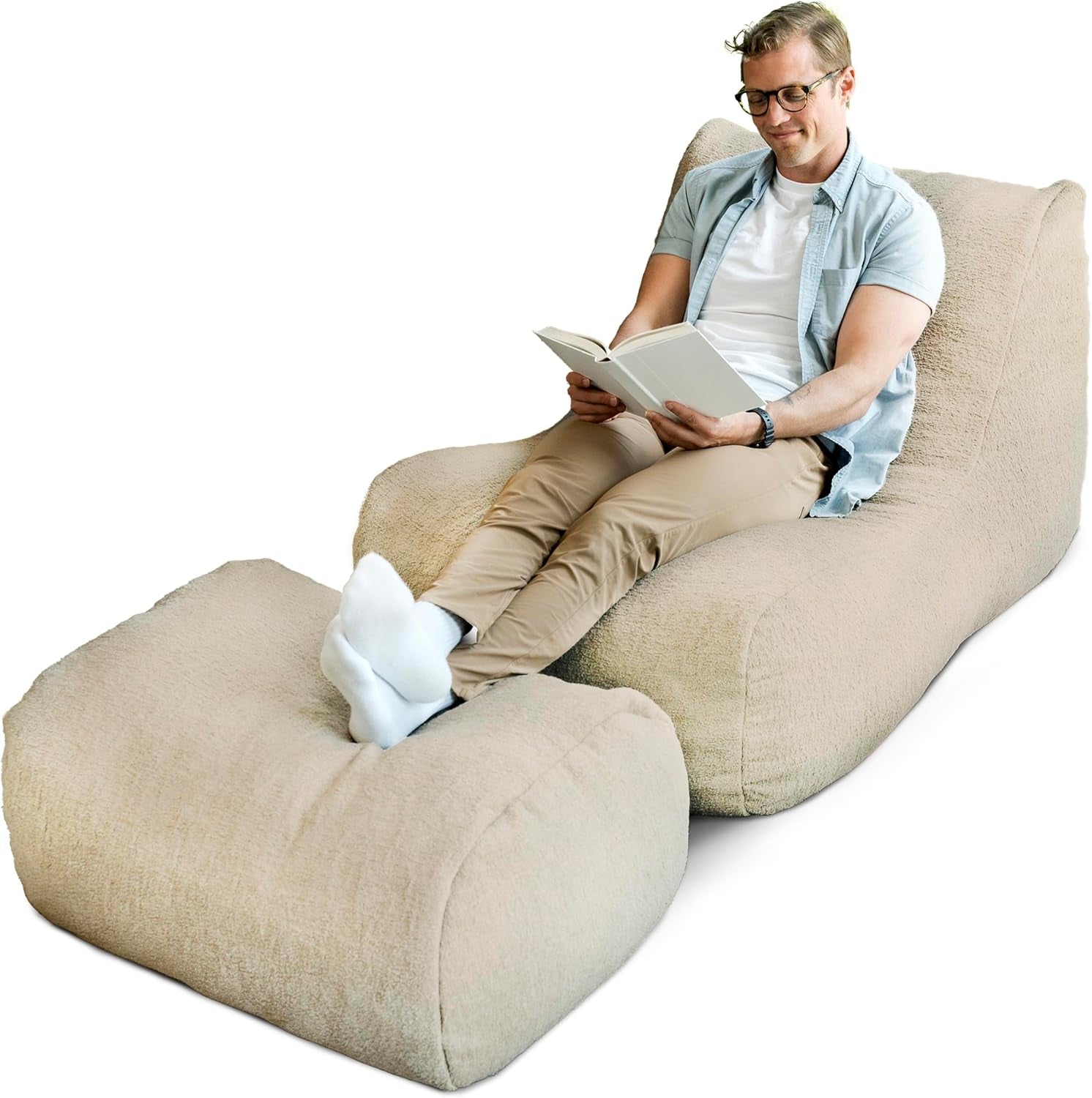 Man wearing glasses reclines on beige fabric lounger reading a book with feet propped on the ottoman