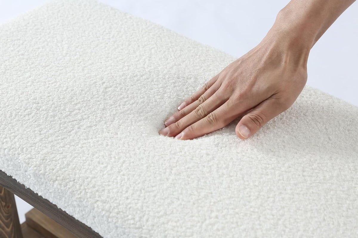 Close-up of a hand pressing into a plush white faux lamb-fur seat top that indents over a wooden bench edge.