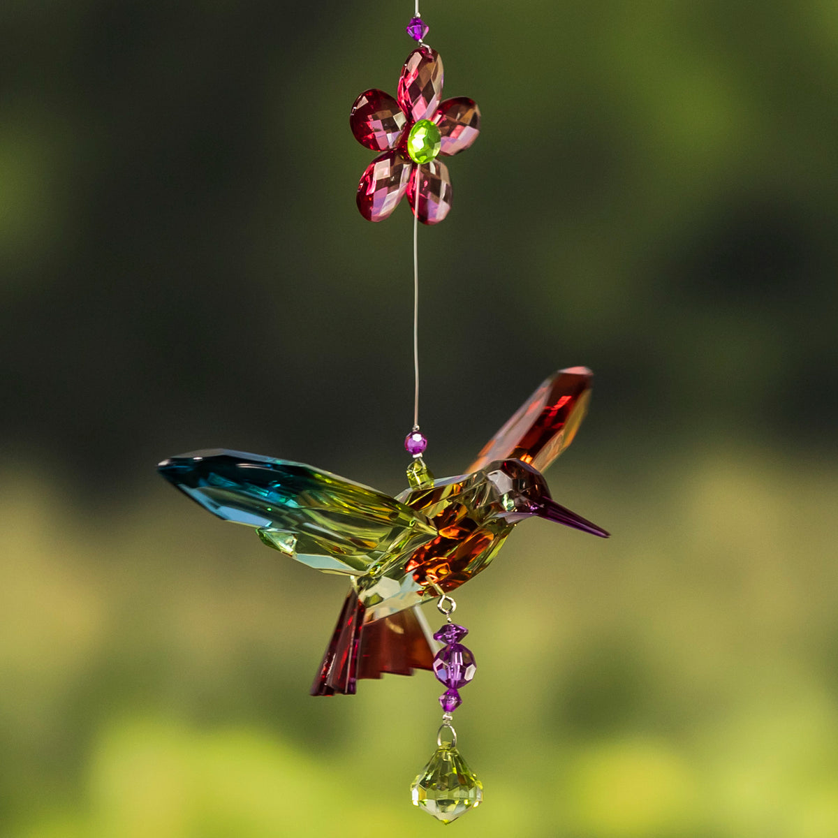 A multicolored faceted hummingbird hangs beneath a pink flower, with beads and a crystal drop.