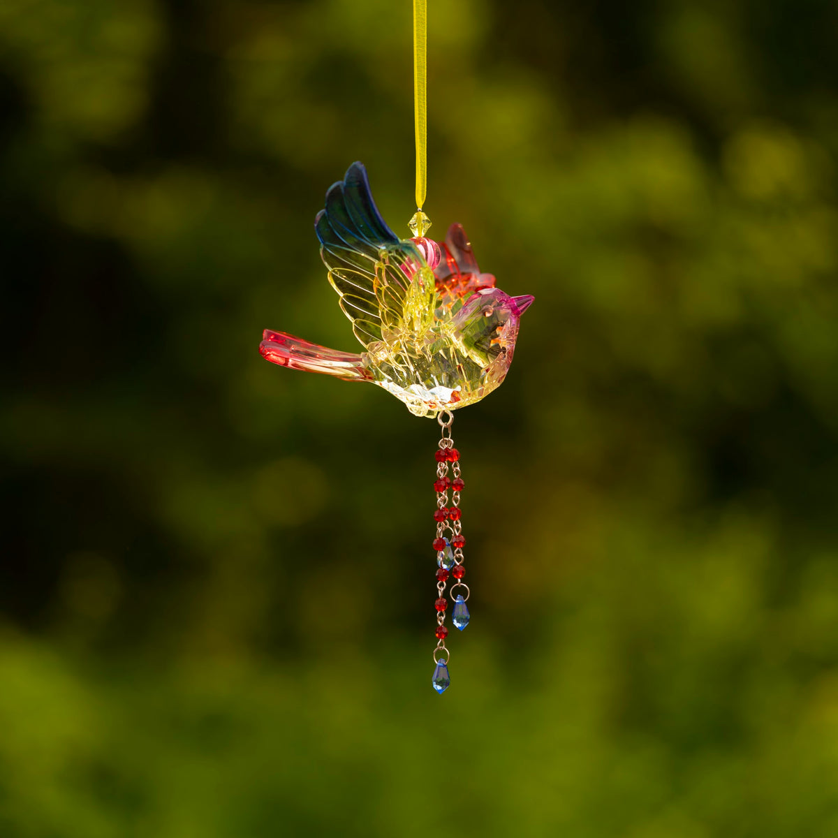 A small colorful bird ornament hangs from a yellow ribbon, with a long chain of beads below.