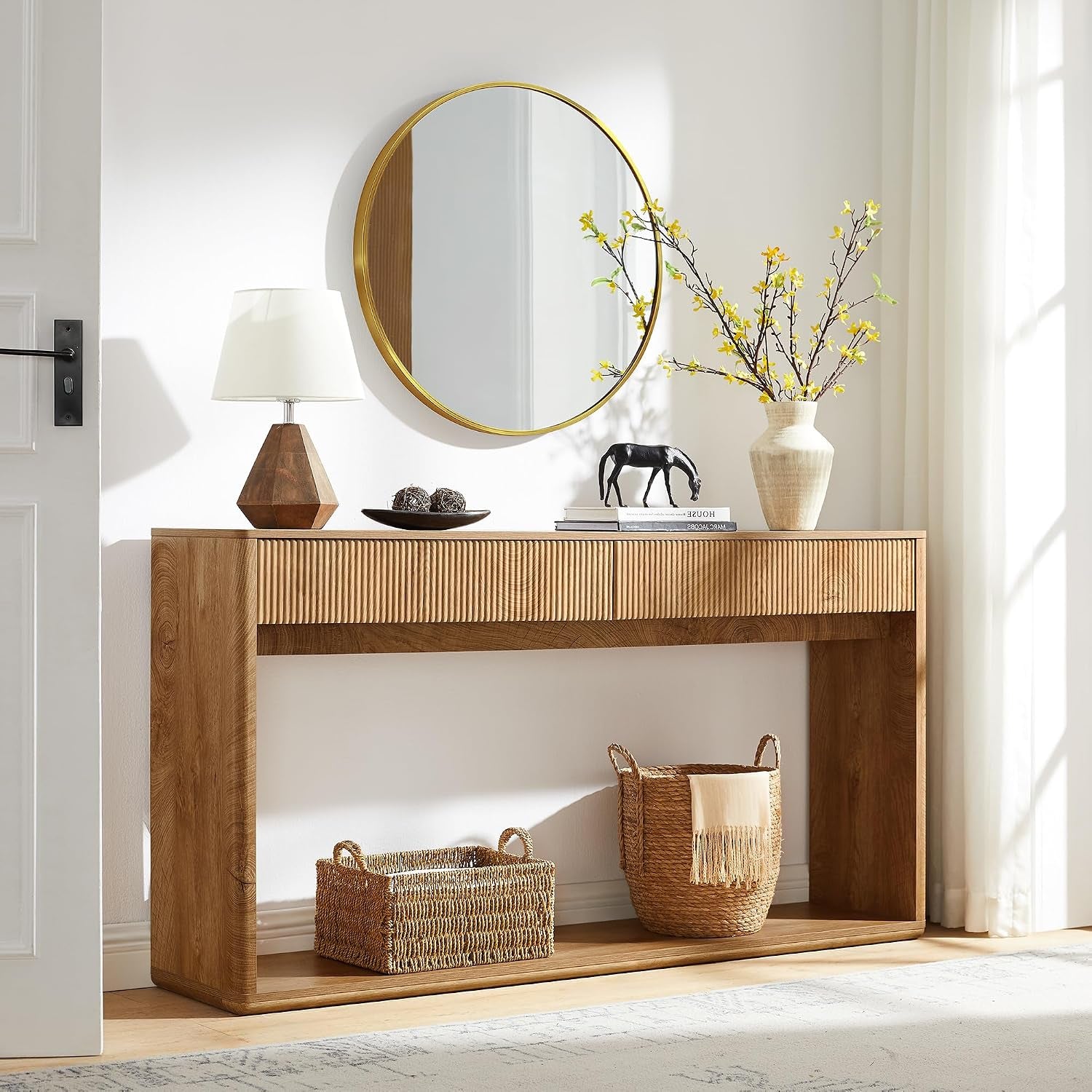 Natural oak console table under a gold-rim round mirror with woven baskets on the lower shelf