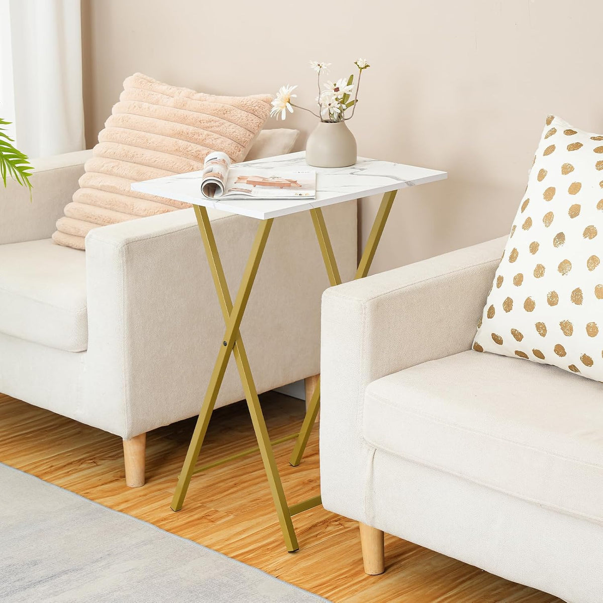 Marble-pattern tabletop with gold folding legs placed between sofas holding a vase and a magazine