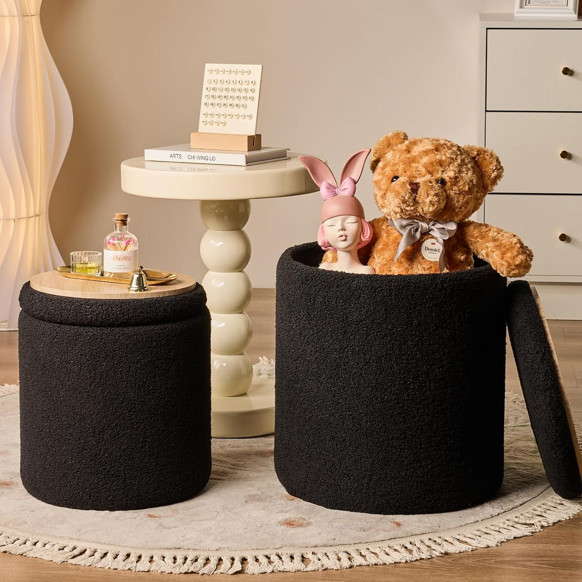 Pair of black round ottomans with one lid off showing stuffed bear and mannequin head in a living room scene