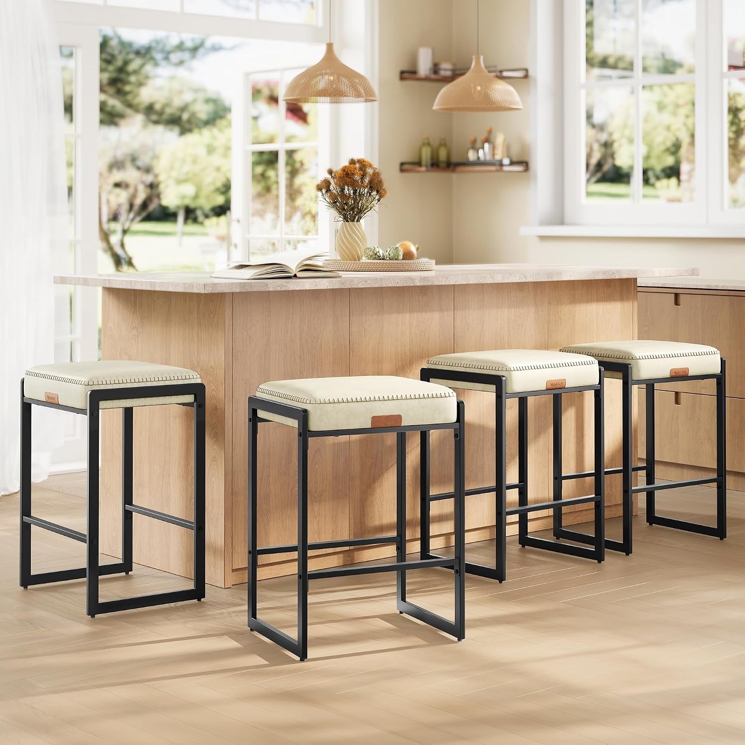 Four cream-colored stools under a sunlit island with large windows and woven pendant lights in the background.