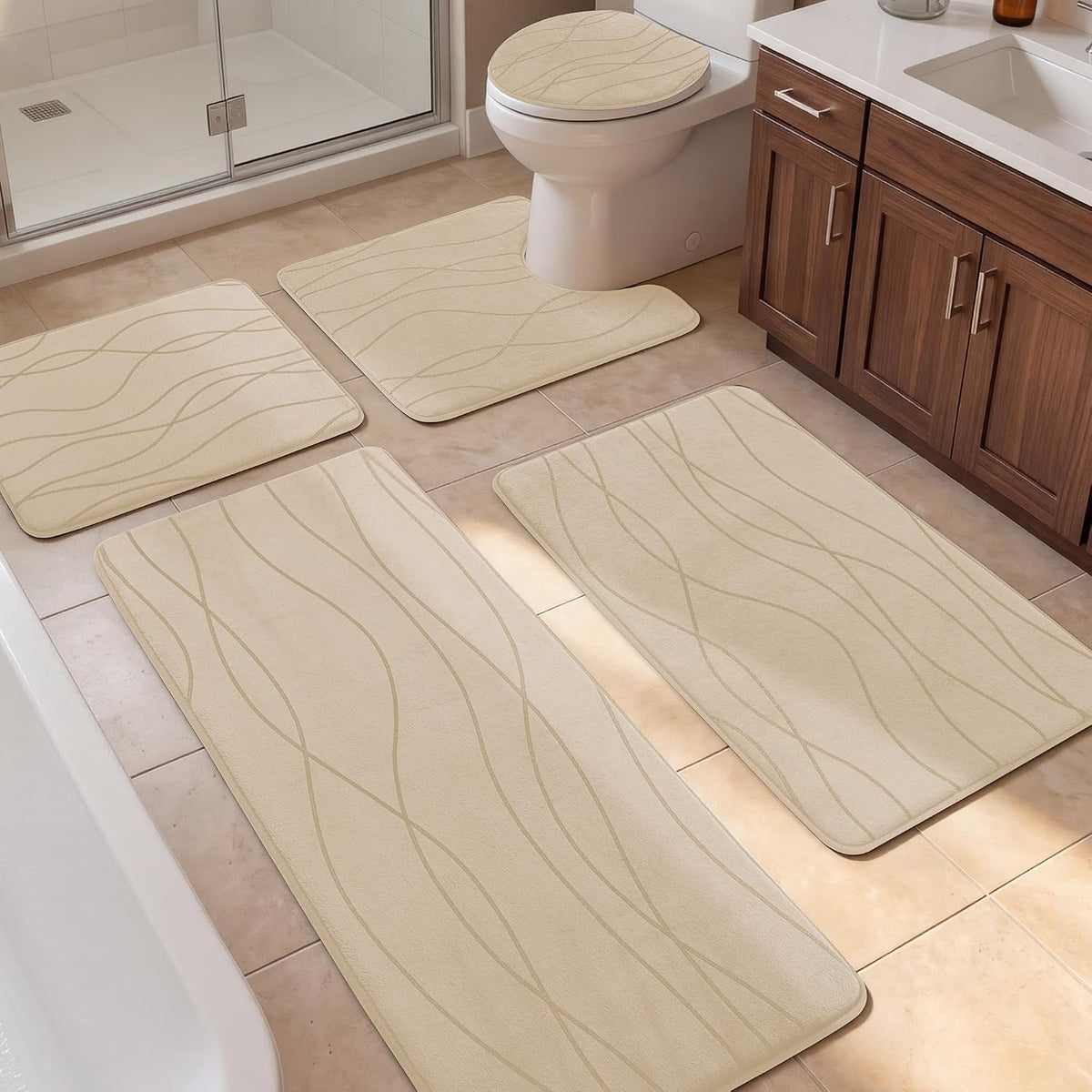 Five beige bath rugs and a toilet seat cover arranged on tiled bathroom floor near shower and vanity.