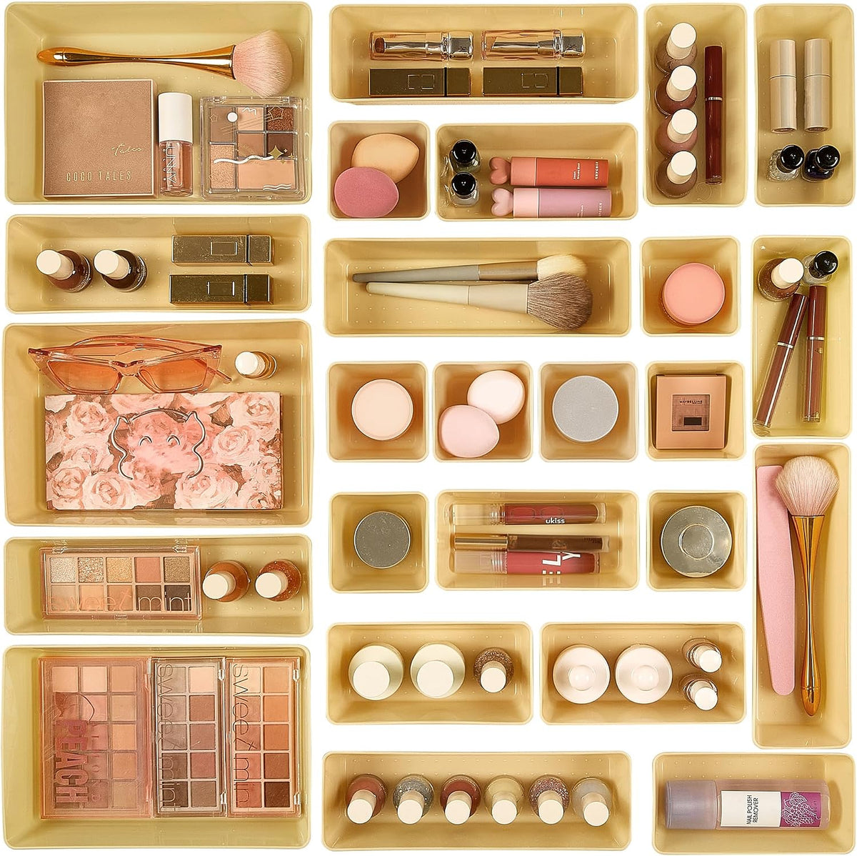 Overhead grid of beige/gold clear trays filled with makeup and brushes